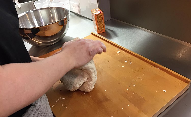 Hands at work kneading dough on bulthaup chopping board.